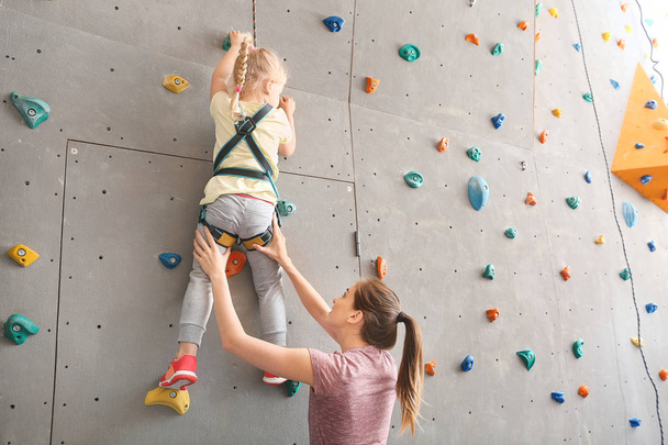 Instructor helping little girl to climb wall in gym - Foto, Imagen