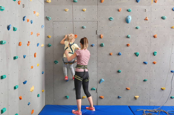 Instructor helping little girl to climb wall in gym - Фото, изображение
