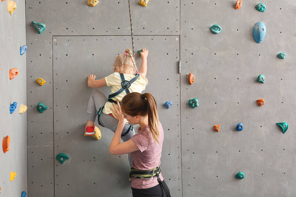 Ausbilder hilft kleinem Mädchen beim Klettern in Turnhalle - Foto, Bild