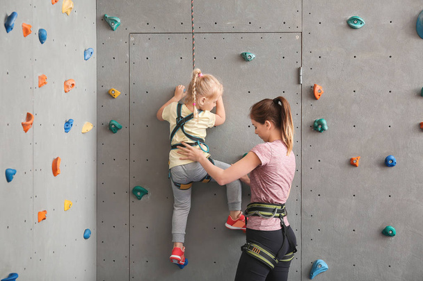 Instructor ayudando a la niña a escalar la pared en el gimnasio
 - Foto, imagen
