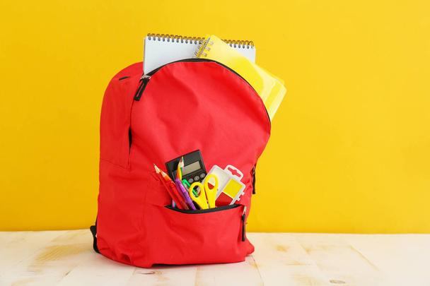 School backpack with stationery on table against color background - Photo, Image