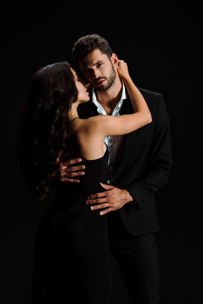 attractive girl hugging handsome bearded man looking at camera isolated on black  - Photo, Image