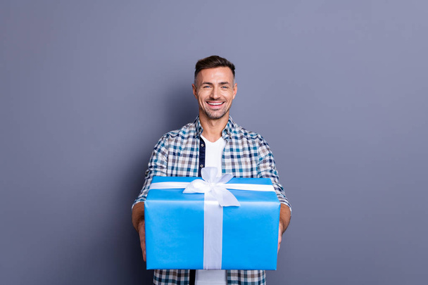 Portrait of his he nice attractive cheery cheerful bearded guy wearing checked shirt holding in hands giving celebratory box isolated over blue violet purple pastel background - Fotoğraf, Görsel