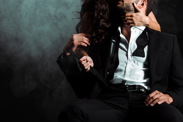 oříznutý pohled ženy stojící a dotýkání vousatého muže na černém s kouřem  - Fotografie, Obrázek