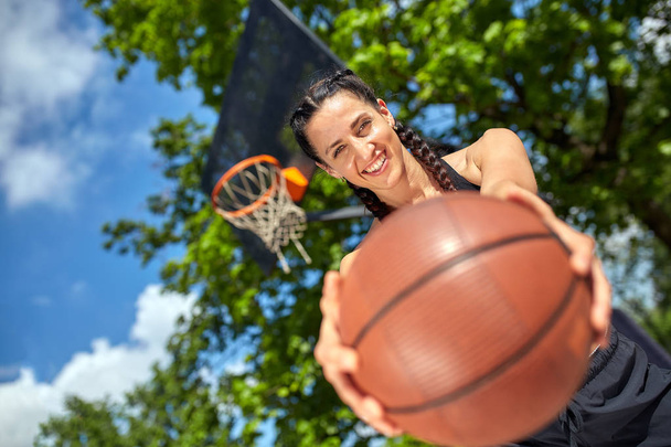 Beautiful, sporty latin girl with a basketball under the ring on a street basketball court. Sport motivation, healthy lifestyle, copy space, advertising banner. - Fotografie, Obrázek