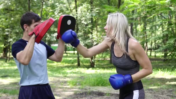 Beautiful woman is engaged in boxing in the park. A woman is boxing with a trainer. - Footage, Video