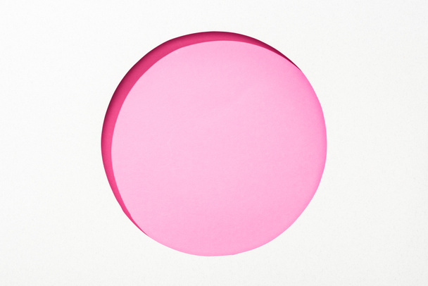 cut out round hole in white paper on pink colorful background - Фото, зображення