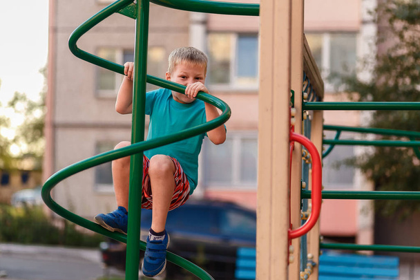 short-haired seven-year-old boy climbs on the Playground near the house in the summer - Valokuva, kuva