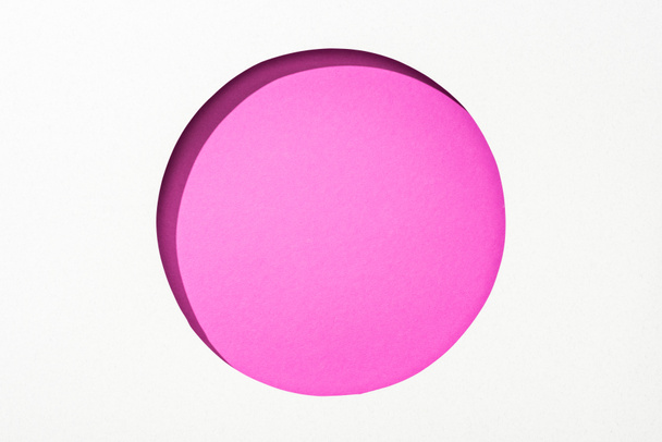 cut out round hole in white paper on bright pink colorful background - Фото, зображення