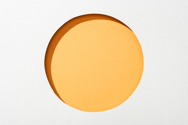 Vystřihněte kulatý otvor v bílém papíře na oranžovém pozadí - Fotografie, Obrázek