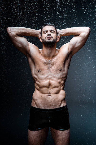handsome wet man looking at camera under raindrops on black  - Foto, immagini