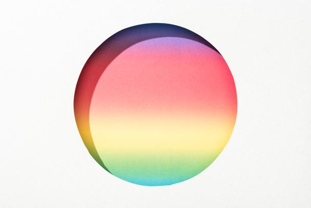 ausgeschnittenes rundes Loch in weißem Papier auf buntem Regenbogenhintergrund - Foto, Bild