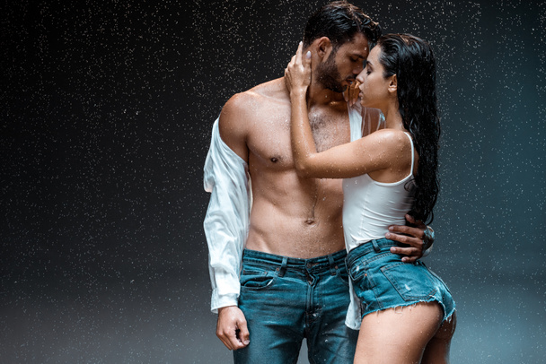 黒の雨滴の下でセクシーな女の子と一緒に立っている服を脱いで筋肉の男  - 写真・画像