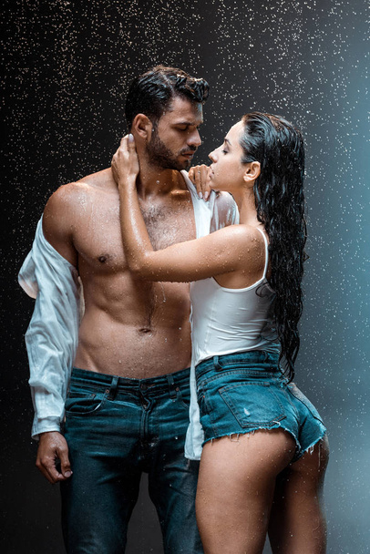 undressed and muscular man standing with sexy girlfriend under raindrops on black  - Fotografie, Obrázek