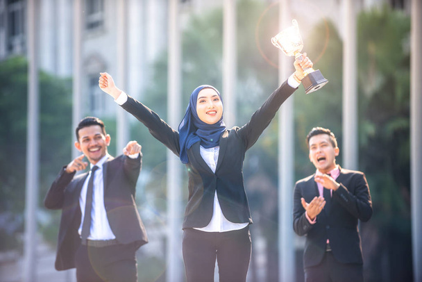 Succesvolle moslim zakenvrouw met armen omhoog houden een trofee a - Foto, afbeelding