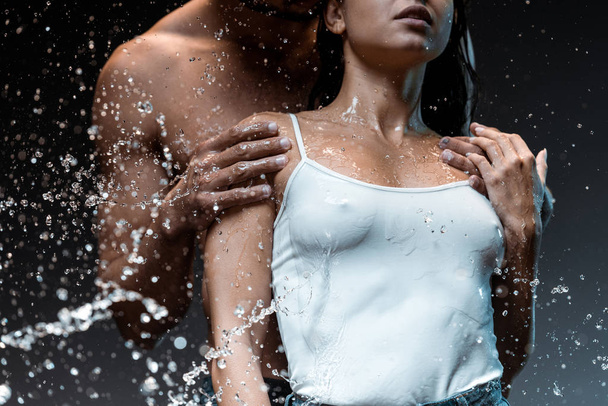 Selektiver Fokus des Mannes umarmt sexy Frau in der Nähe von Wasserspritzern auf Schwarz  - Foto, Bild