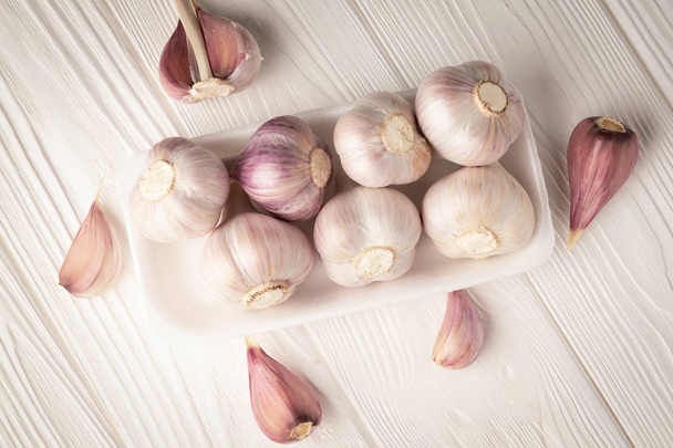 Top view garlic heads in a plastic container on a white wooden table - Foto, imagen