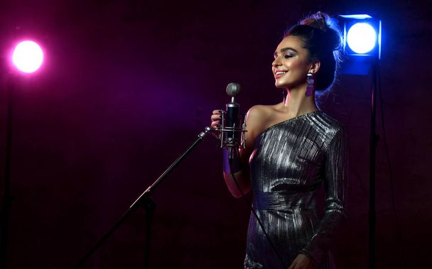 Beautiful singing girl curly afro hairstyle. Beauty woman singer sing with microphone karaoke song  blue and pink neon spotlights - Foto, imagen