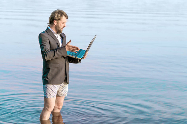 Un homme en colère dans une veste et sous-vêtements avec un ordinateur portable à la main est
  - Photo, image