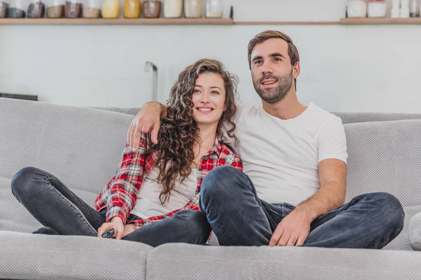 Beautiful girl and a young man sitting on the couch and watch TV. People relax on the couch.Young man in glasses and blue shirt.Young woman with glasses. - Photo, Image