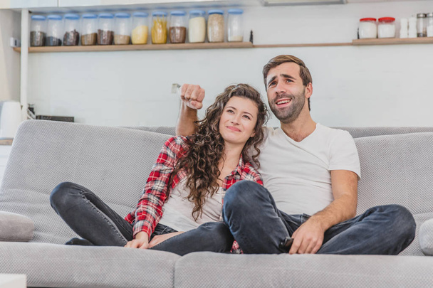 Beautiful girl and a young man sitting on the couch and watch TV. People relax on the couch.Young man in glasses and blue shirt.Young woman with glasses. - Fotoğraf, Görsel