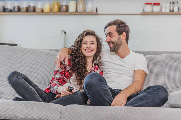 Beautiful girl and a young man sitting on the couch and watch TV. People relax on the couch.Young man in glasses and blue shirt.Young woman with glasses. - 写真・画像