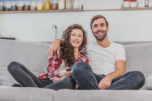 Beautiful girl and a young man sitting on the couch and watch TV. People relax on the couch.Young man in glasses and blue shirt.Young woman with glasses. - Φωτογραφία, εικόνα