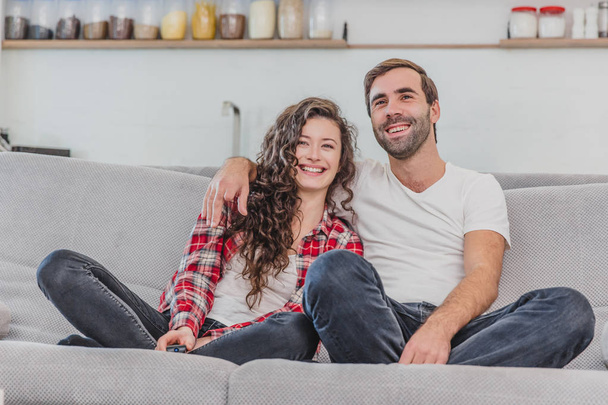 Beautiful girl and a young man sitting on the couch and watch TV. People relax on the couch.Young man in glasses and blue shirt.Young woman with glasses. - Φωτογραφία, εικόνα