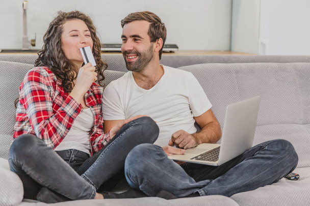 Una buona coppia mentre fa shopping online usando un computer portatile e sorridendo seduto su un divano a casa
. - Foto, immagini