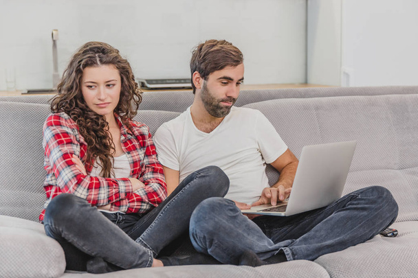 A good couple while shopping online using a laptop and smiling while sitting at a couch at home. A woman was offended by a man because he did not make her purchase online. - 写真・画像