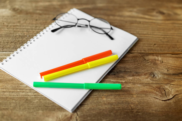 Green, yellow and orange markers, a notebook and glasses on a wooden background. The concept of school, creativity, childhood. - Photo, Image