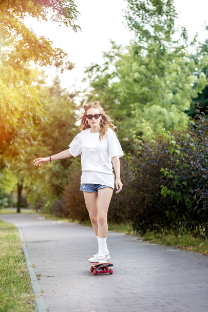 Giovane ragazza adolescente cavalcando uno skate board nel parco. Il concetto di stile di vita, tempo libero
. - Foto, immagini