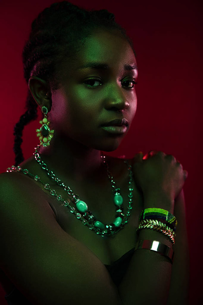 Kleurrijk en creatief portret van mooie donkere Afrikaanse vrouw op rode achtergrond - Foto, afbeelding