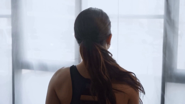 όμορφη αθλητική γυναίκα περπάτημα στο γυμναστήριο, κοιτάζοντας μέσα από τα παράθυρα και στη συνέχεια κοιτάζοντας την κάμερα  - Πλάνα, βίντεο
