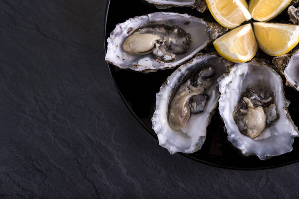 Oysters plate with lemon on grey background. Served table with oysters and lemon. Fresh oysters close-up top view. Healthy sea food. Oyster dinner with champagne in restaurant. Gourmet food. Sea food - Photo, Image