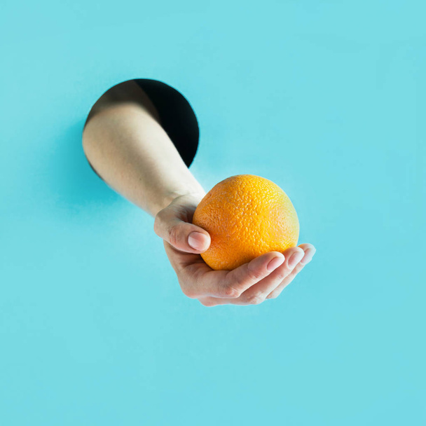 Female hand holding ripe orange in paper hole. - Фото, зображення