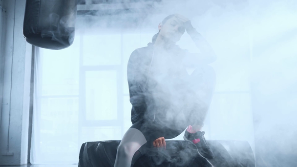 hoodie güzel sporcu lastik üzerinde oturan ve dumanlı jimnastik kamera bakıyor - Video, Çekim