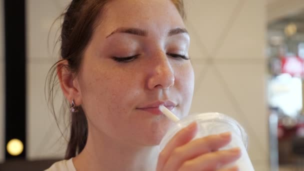 Portret van jonge vrouw is het drinken van milkshake van stro in Fast food café. - Video