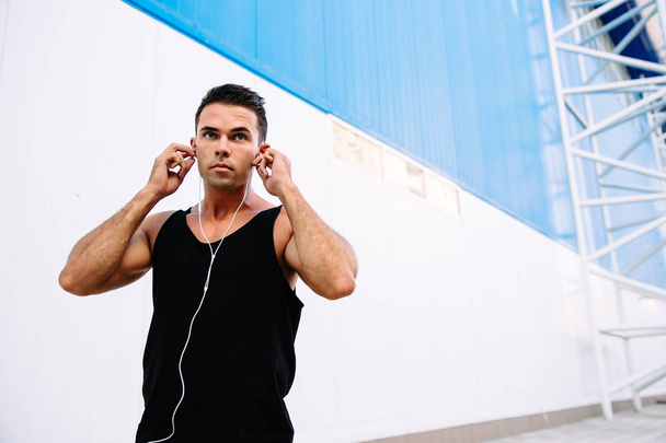 Attractive sportsman plugging headphones into the ears - Foto, Imagem