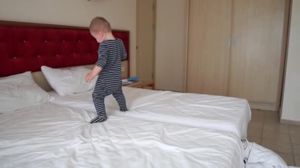 Un chico lindo juega alegremente, cae en una cama grande en una habitación de hotel, cámara lenta
 - Metraje, vídeo