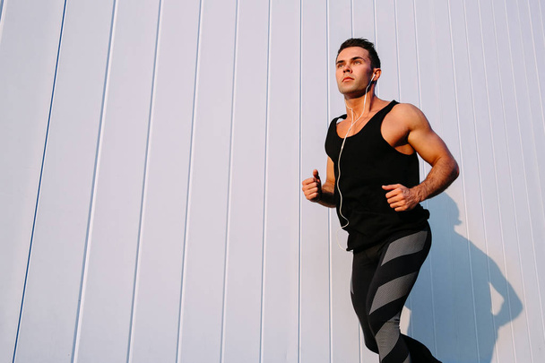 Muscular man running against the white wall, outdoors - Фото, изображение