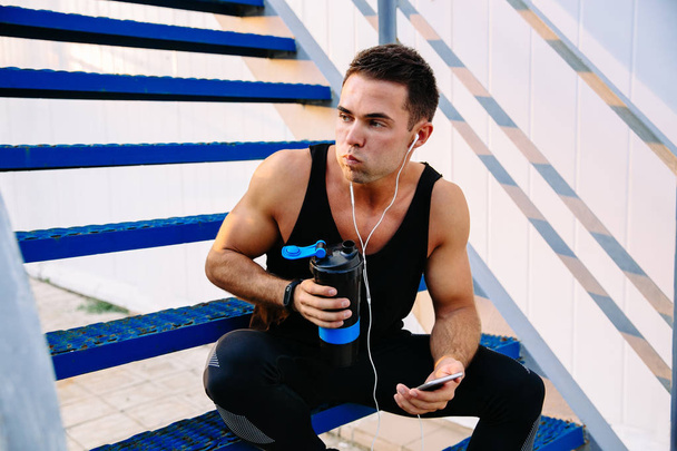 Attractive sportsman drinking a water after workout, outdoors - Фото, изображение