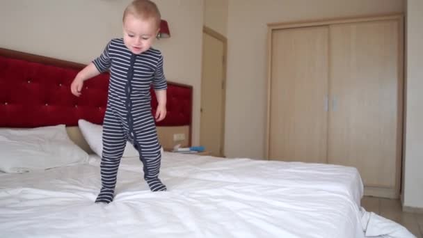 Roztomilý blonďatý batole šťastně skáče na velkou postel v hotelovém pokoji v pomalém pohybu - Záběry, video