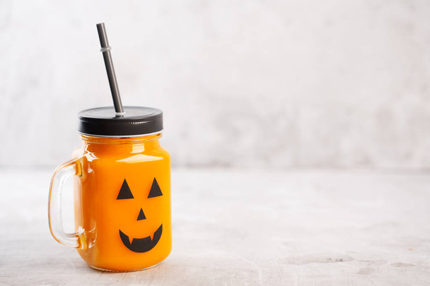 Halloween healthy pumpkin or carrot drink in the glass jar with scary face on a gray background - Φωτογραφία, εικόνα