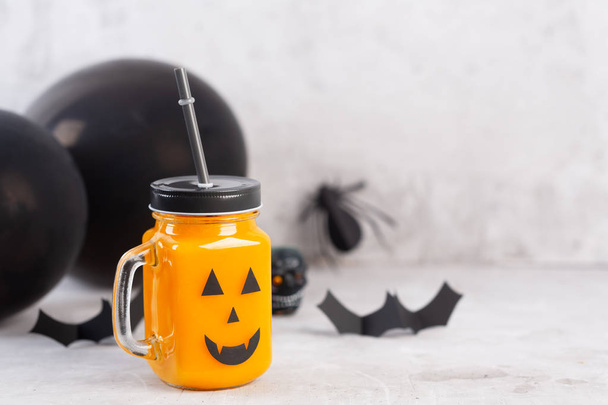 Halloween healthy pumpkin or carrot drink in the glass jar with scary face on a gray background - Foto, Imagem
