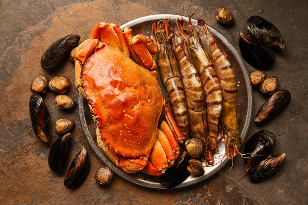 vue de dessus du crabe et des crustacés crus dans un bol près des coques et des moules éparpillées sur la surface texturée
  - Photo, image