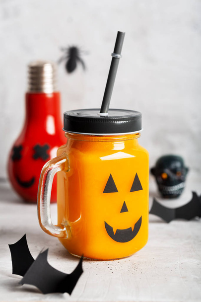 Halloween healthy pumpkin or carrot and tomato drinks in the glass jar with scary face on a gray background - Фото, зображення