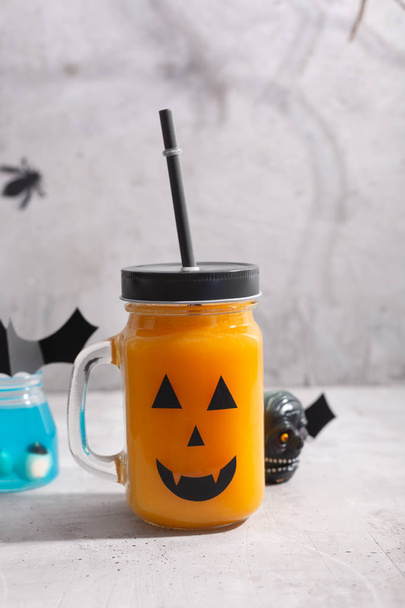 Halloween healthy pumpkin or carrot drink in the glass jar with scary face on a gray background - Foto, Bild