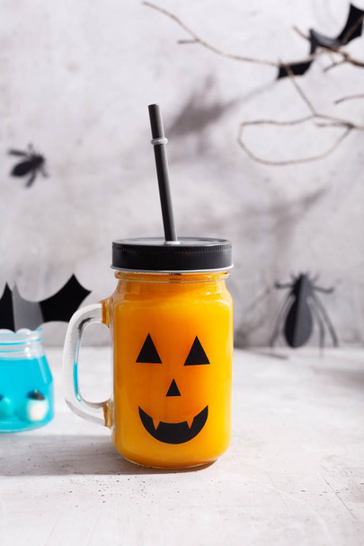 Halloween healthy pumpkin or carrot drink in the glass jar with scary face on a gray background - Foto, afbeelding