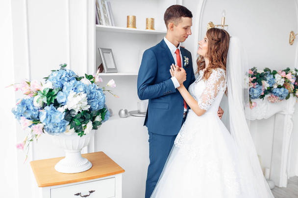 Beautiful bride in white dress and groom in suit, posing in white Studio interior, wedding - Photo, Image